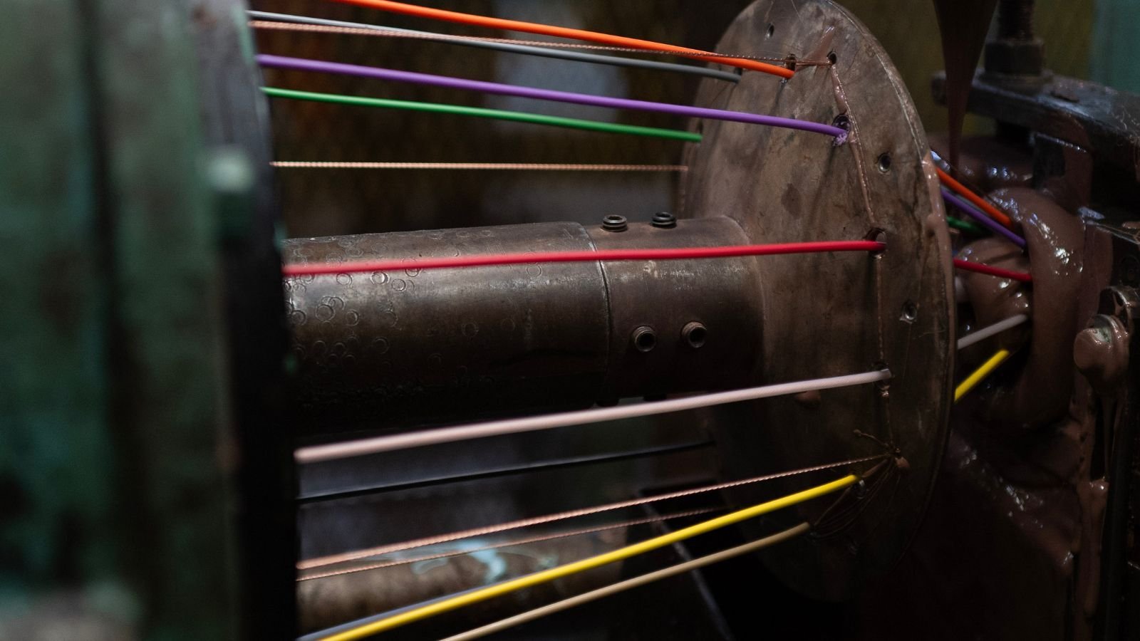 Close-up of a machine with colorful threads—red, yellow, purple, orange, and white—stretched across a metal spindle, conveying a sense of industrial creativity.
