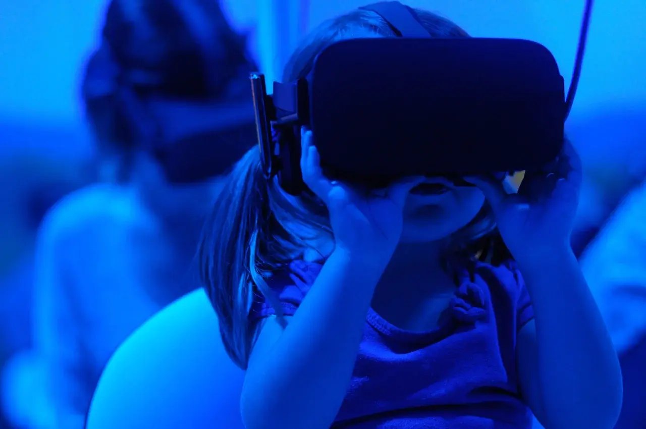 A young girl with pigtails wears a VR headset, immersed in a virtual experience, illuminated by a cool blue light.