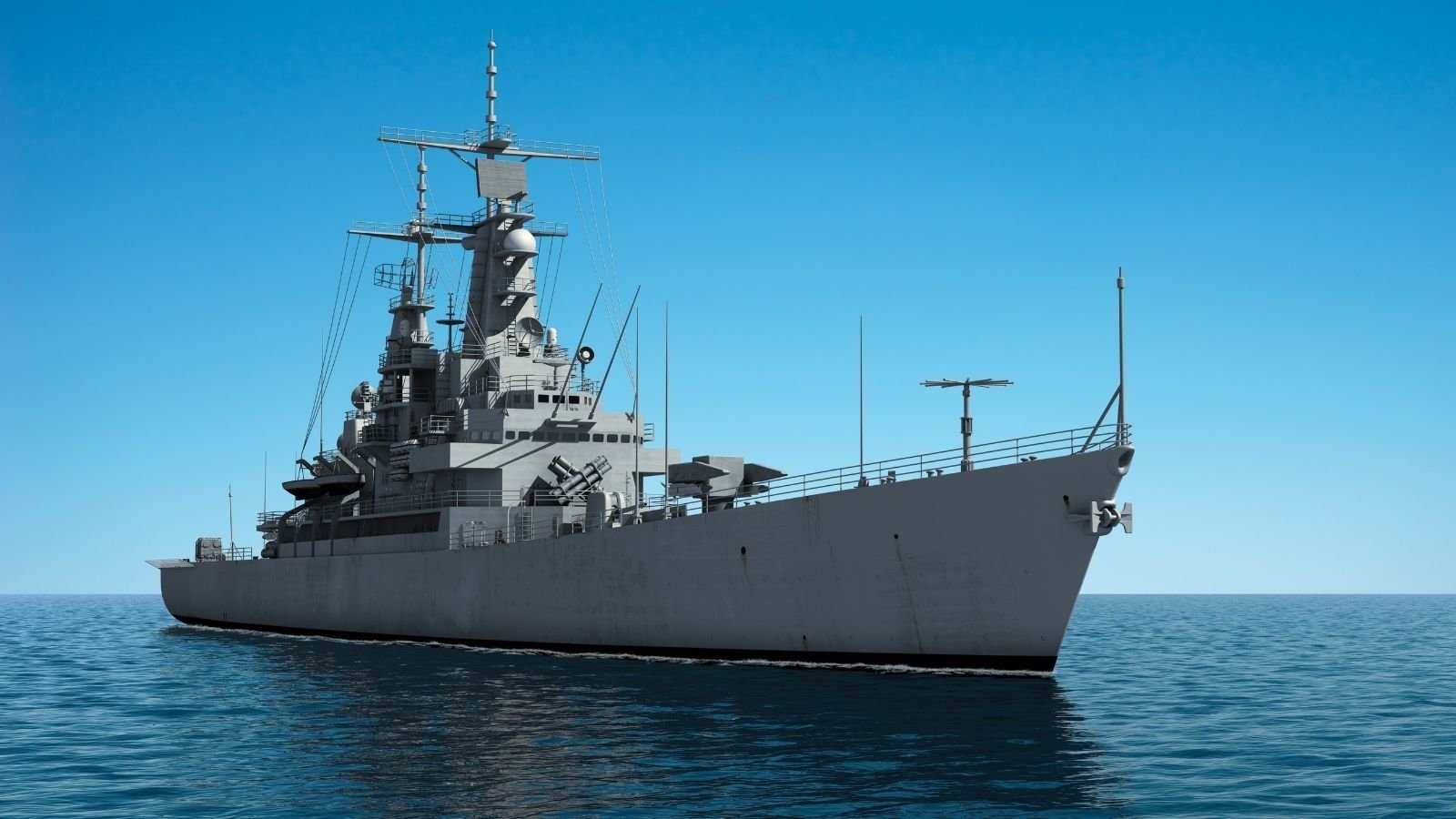 A large naval battleship navigates through calm ocean waters under a clear blue sky, showcasing its impressive radar equipment and towering structure.