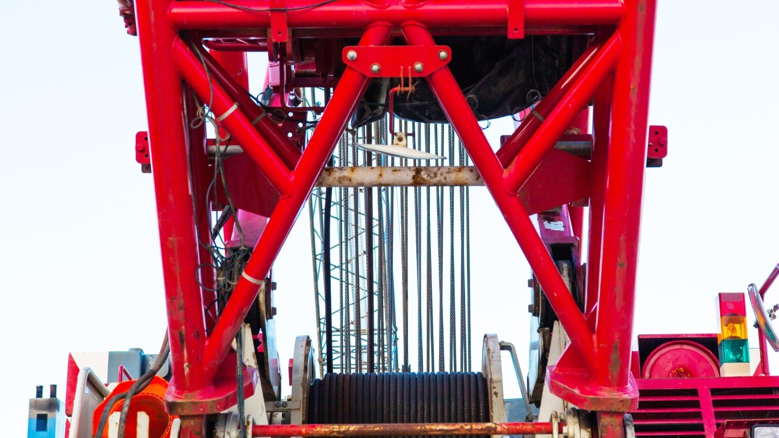 Close-up of a red crane mechanism with cables and pulleys against a clear sky.