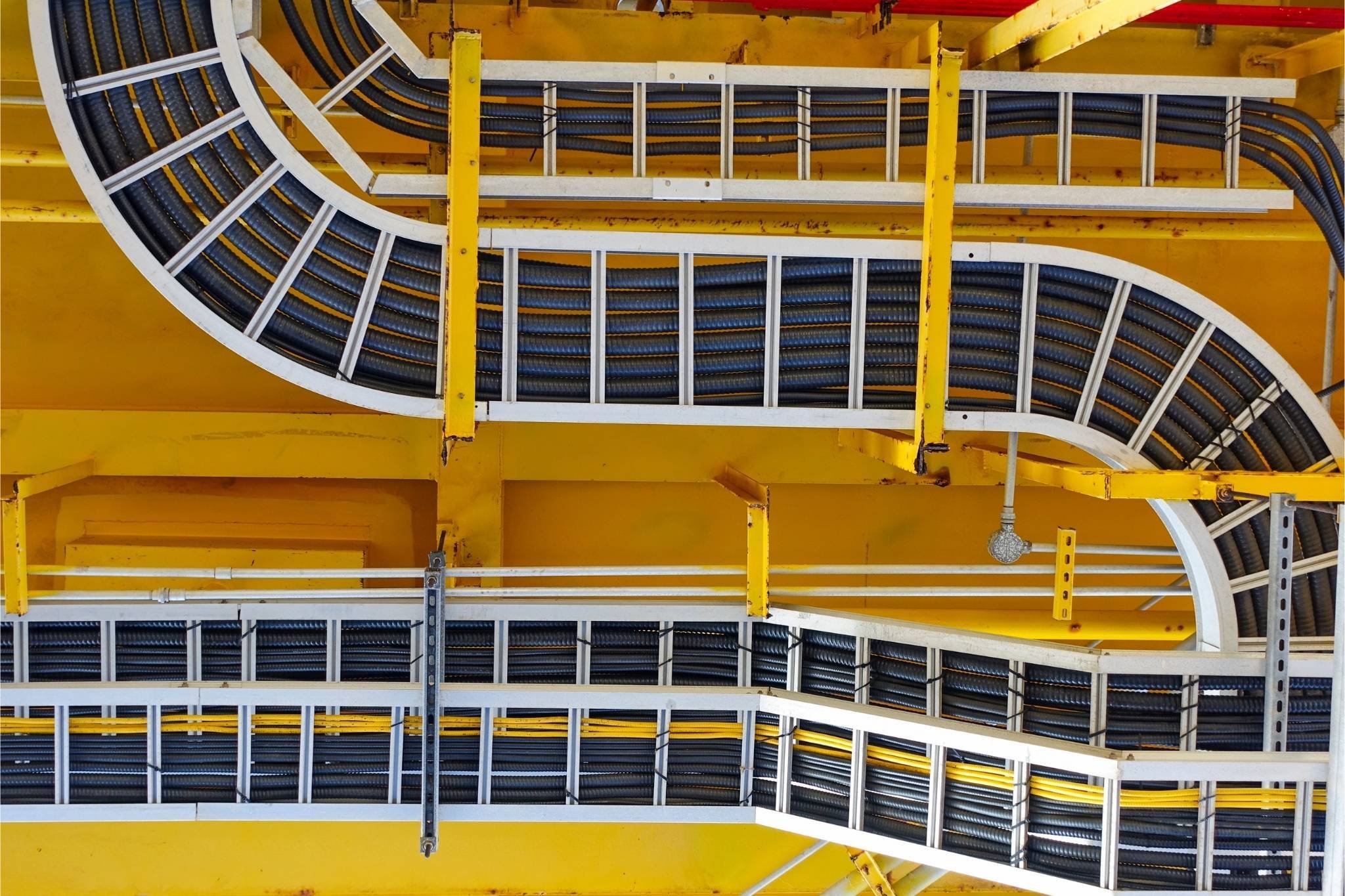 Yellow industrial ceiling with neatly arranged curved cable trays and black cables.