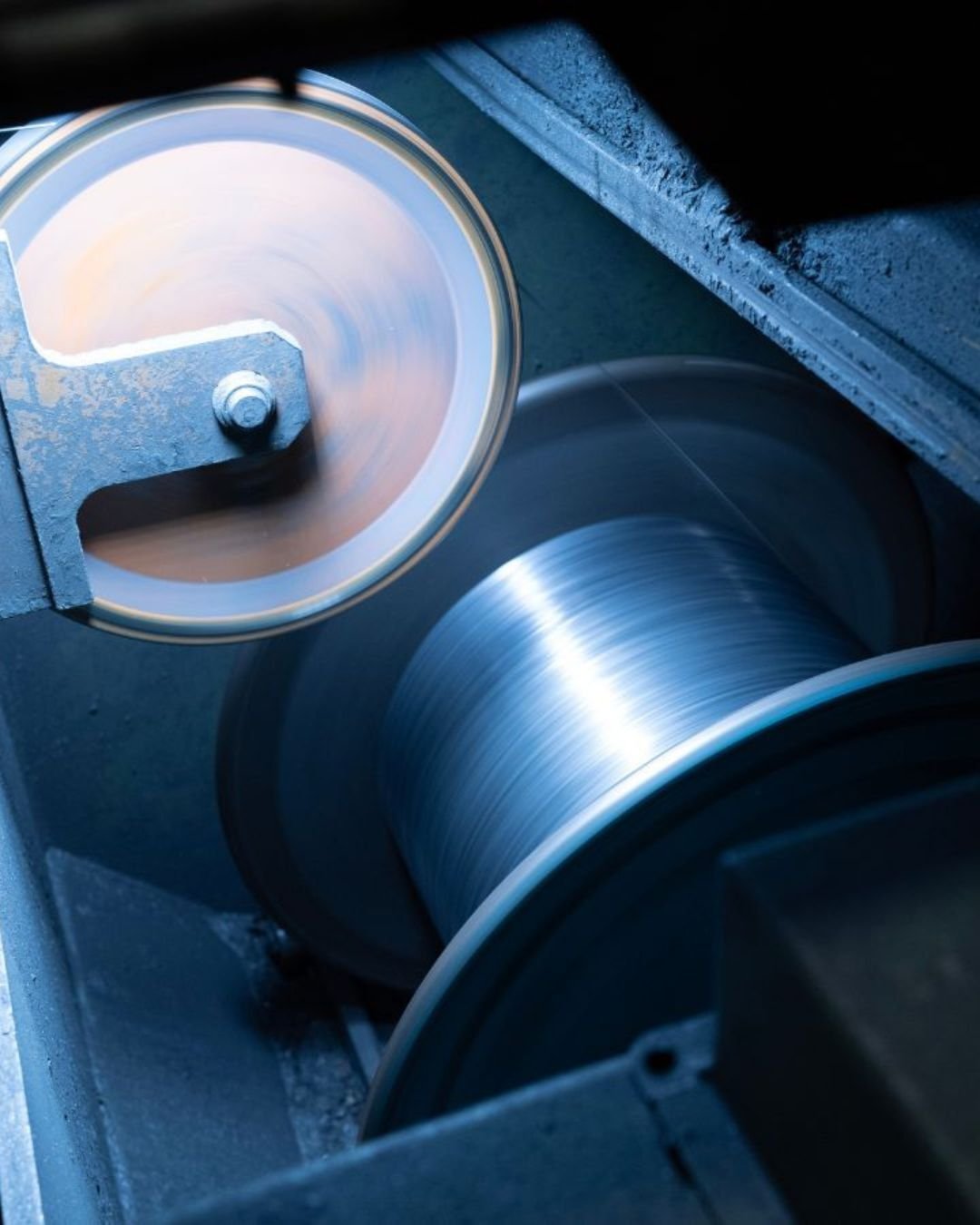 Close-up of spinning industrial machinery with metallic spools and a glowing wheel, conveying motion and precision in a dimly lit setting.