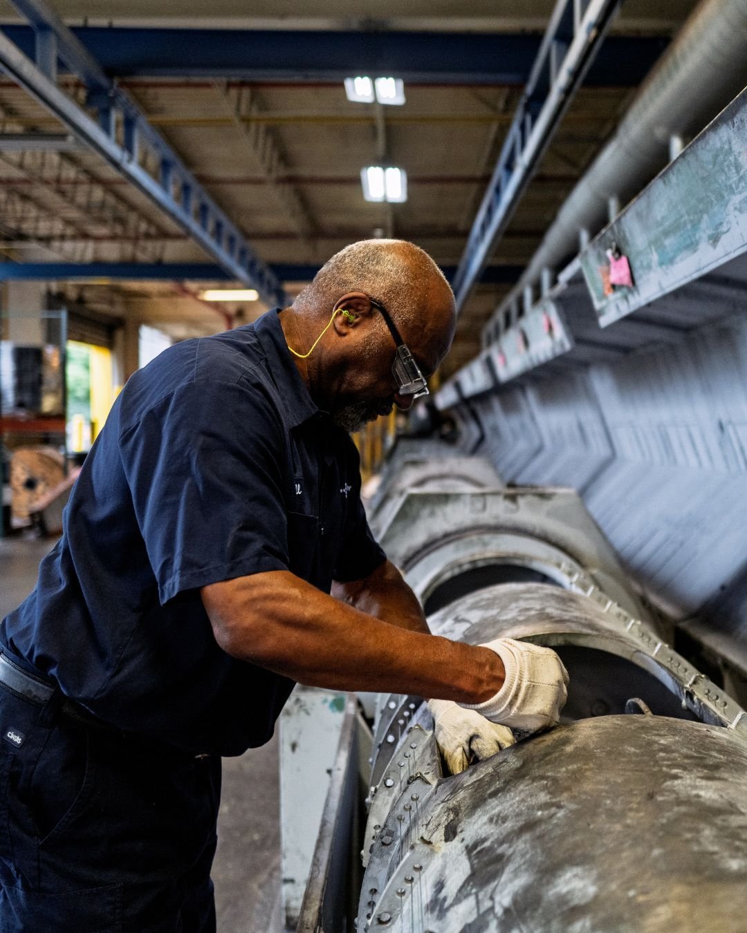 A worker in protective gear inspects industrial machinery inside a factory.