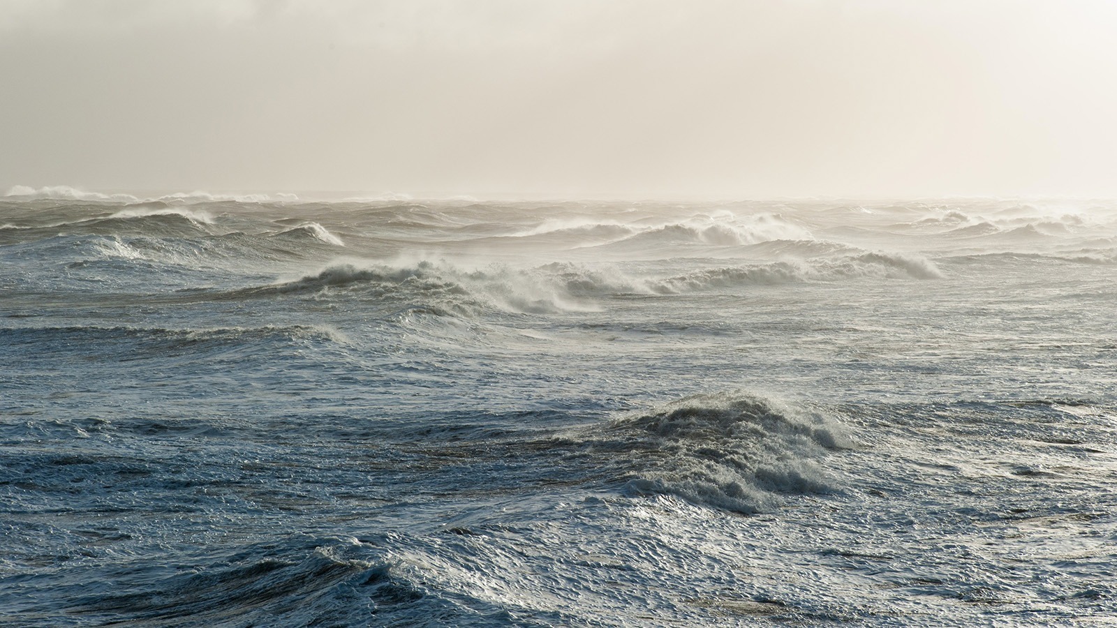 Rough ocean waves under a clouded sky, with high winds.