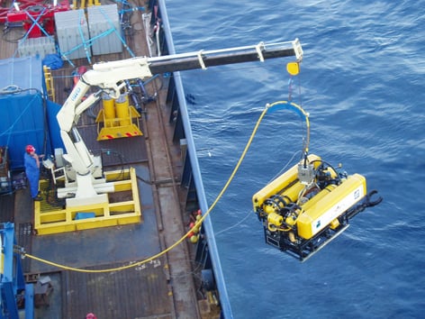 A yellow ROV is being lowered into the ocean by a crane on a ship's deck.