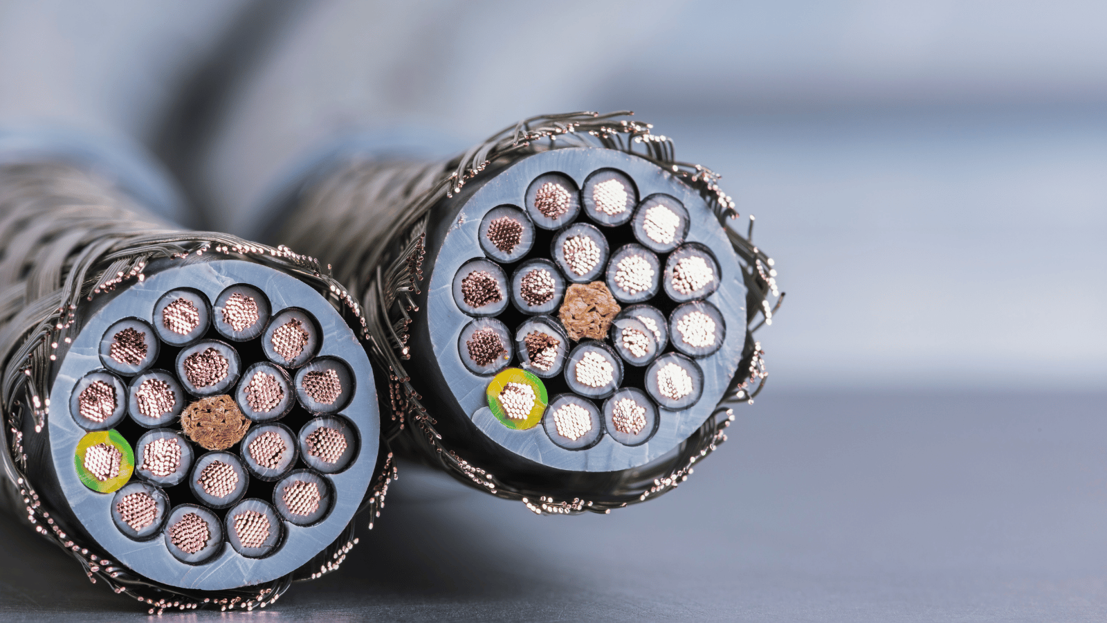 Close-up of two thick, multi-strand cables with silver and copper wires exposed at the ends, resting on a smooth surface. 